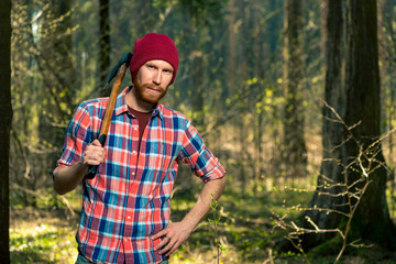 Naklejka na ściany i meble portrait of a forester with a beard and an ax in a shirt in the woods