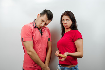 Fototapeta premium Family quarrel, wife scolds her husband, young, beautiful wife beats her husband with a stick. The concept of the psychology of family relations, marriage, domestic conflicts, domestic violence.