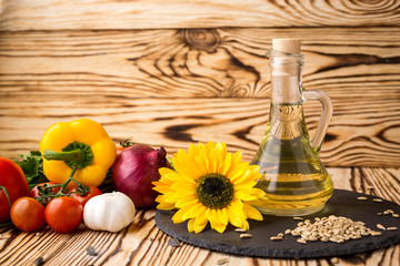 Glass bottle of sunflower oil on a wooden table with a composition of vegetables and seeds