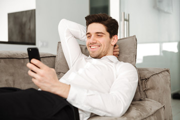 Cheerful young businessman in home lies on sofa