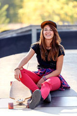 Fototapeta na wymiar Cute urban girl skater sitting on ramp at the skate park enjoying outdoors