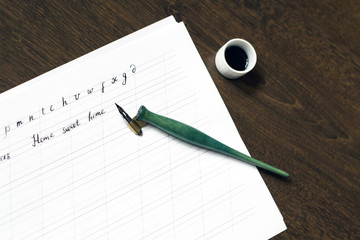 Phrase written on a paper sheet and a green nib for calligraphy