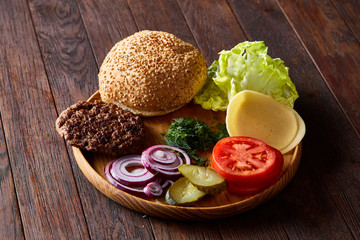 Yummy hamburger ingredients artistically organized on wooden plate, close-up, top view, selective focus