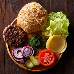 Yummy hamburger ingredients artistically organized on wooden plate, close-up, top view, selective focus