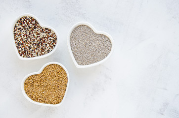 Chia quinoa mix and linseed in heart shaped bowls on a white vintage wooden background surface