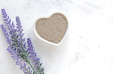 White chia seeds in a heart bowl on vintage white surface and lavander decoration