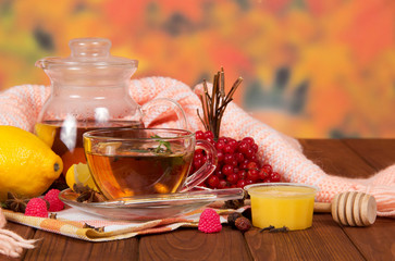 Pitcher and cup of tea, berries, fruit, honey, warm scarf and thermometer on wooden table