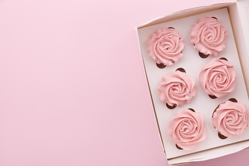 Muffins or cupcakes with flower shaped cream in box on pink background, top view