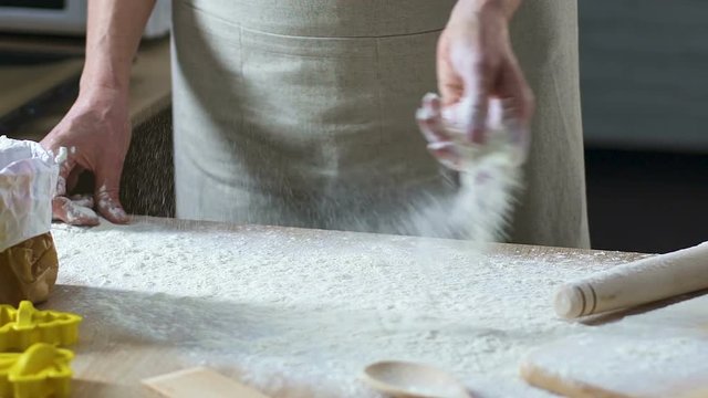Hands of female cooker preparing working place and sprinking flour on table