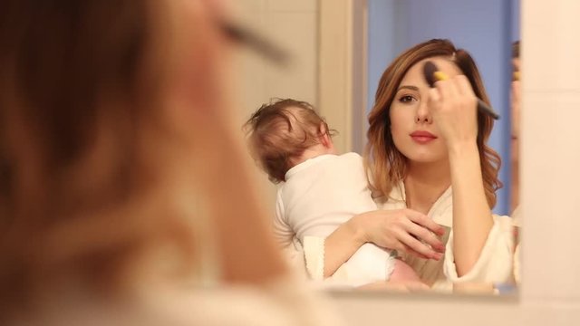 mother holding a litle baby and appying cosmetics