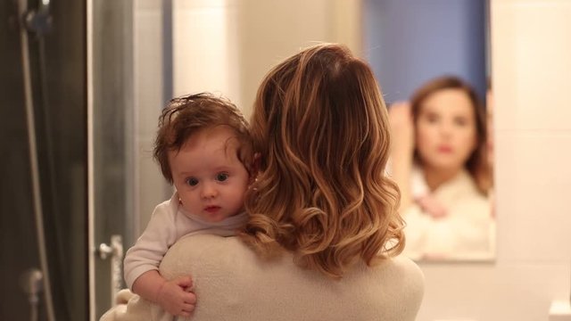 mother holding a litle baby and appying cosmetics