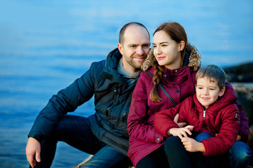Fototapeta premium family mom, dad and son sitting on the beach by the sea. Season - spring, autumn. The concept of family happiness