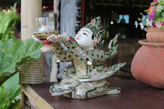 Sitting deva wood carving is holding a lantern on the table.