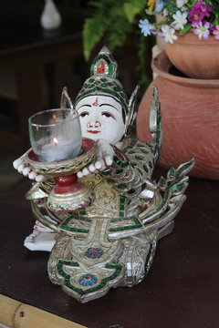 Sitting deva wood carving is holding a lantern on the table.
