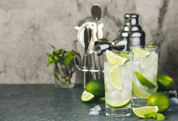 Mojito cocktail with lime and mint in glass on a stone table. Bar tools and ingredients for cocktail.