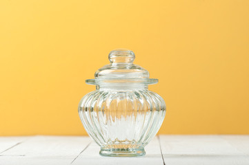 Glass jar with a lid on a white table near the yellow wall..