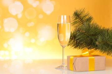 Christmas pine branch, glass of champagne and gift box with beautiful bow, on yellow background