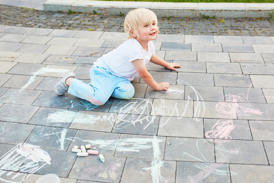 Little boy drawing with chalks on asphalt