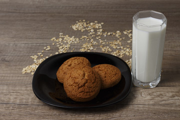 three oatmeal cookies lie on a black plate, oatmeal is scattered
