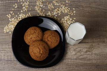 three oatmeal cookies lie on a black plate, oatmeal is scattered