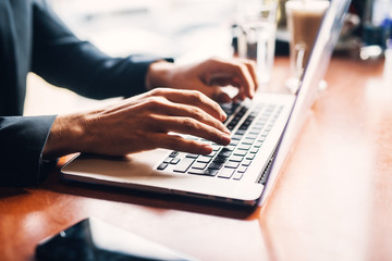 Close up focus view of young businessman in suit typing on a laptop keyboard at the office desk.