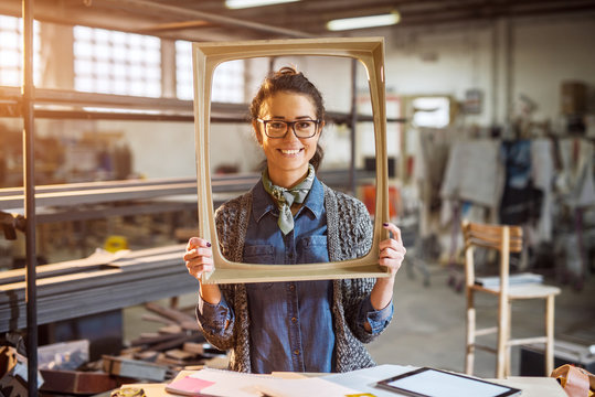Excited middle-aged engineer holding old fashion picture frame in sunny fabric workshop and posing behind.