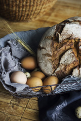 Loaf of rye bread in a basket with chicken eggs on the table