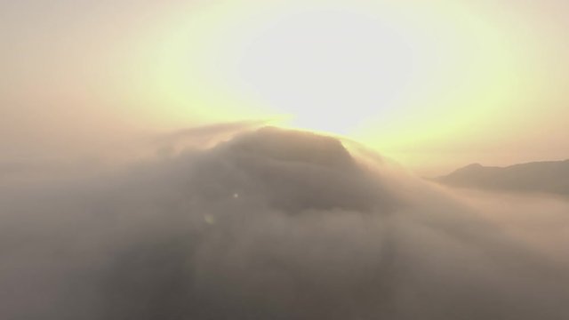 aerial shot of sunrise over the mountain peak covered by the cloud camera moving from right to left