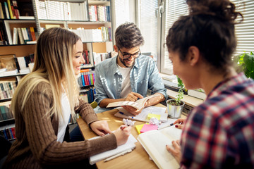 Group of satisfied smiling students study together at the library desk.