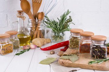 Kitchen utensils, herbs, colorful dry spices in glass jars on white  background