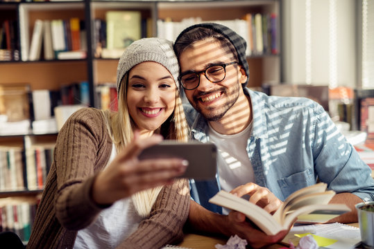 Lovely happy young school love couple taking a selfie while study together in the library.