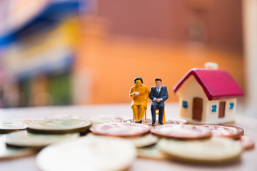 Miniature people, man and woman sitting on stack coins and mini house background using as job retirement, family life and insurance concept