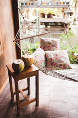 Hammock with colorful pillows and wooden table with two fresh coconuts. Wooden house