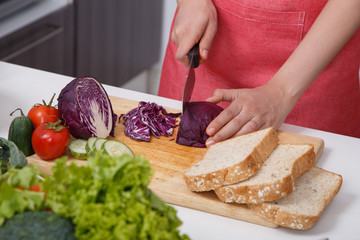 hand cutting purple cabbage on board in kitchen room