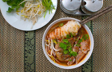Asian spicy noodle soup with chopstick hold on noodle with pork bone and fresh vegetable on bamboo wicker thai  style, home made, hot and spicy noodle soup, asian food.