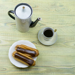 Eclairs and coffee on a wooden background.