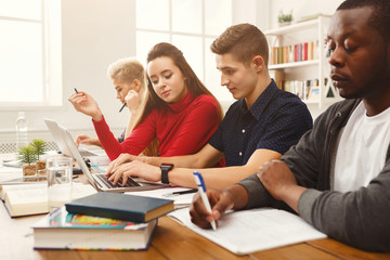 Group of diverse students studying at wooden table