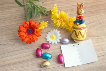 Easter greeting card with colored eggs candies, ceramic rabbit and flowers, on wood table with Copy space background.