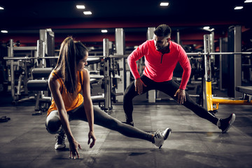 Attractive young shape girl doing workouts with her personal trainer in the modern gym.