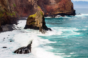 Blue ocean waves crashing on a rock near rocky coast line in Madeira island, Portugal