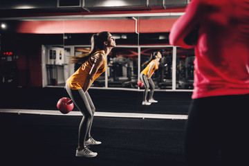 Side view of attractive sexy girl doing exercises with a kettlebell in front of the mirror and personal trainer.