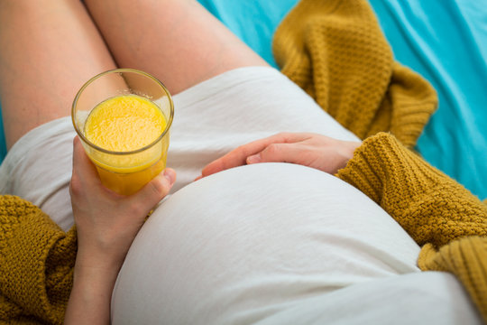 Pregnant woman drinking orange juice. Aerial close up view.