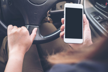 Mockup image of a hand holding and using white mobile phone with blank black desktop screen while driving car on the road