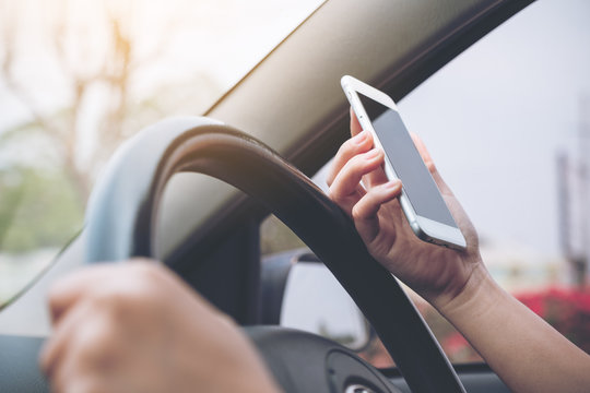 Closeup image of a hand holding and using mobile phone while driving car on the road