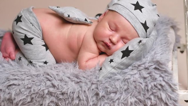 Adorable newborn baby boy in grey pyjamas curled up on grey blanket