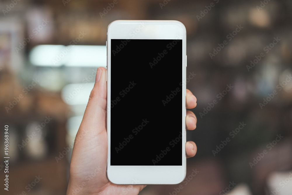 Wall mural mockup image of a hand holding white mobile phone with blank black desktop screen with blur backgrou