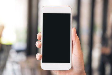 Mockup image of a hand holding white mobile phone with blank black desktop screen with blur background