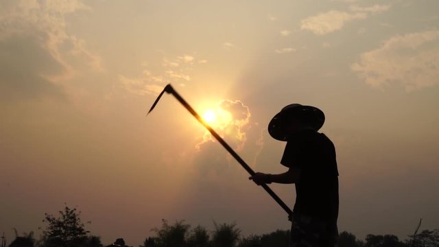 Agriculture life Concept : Black silhouette of a worker or gardener holding spade is digging soil at sunset light, Slow motion shot
