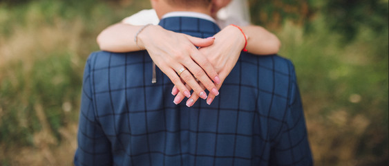 Wedding ring on the finger of the bride. The newlyweds turned away and kiss.