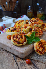 Small pizza with mozzarella cheese, ham, basil, cherry tomatoes. Buns of yeast dough on wooden background. Mini pizzas. Homemade baking.